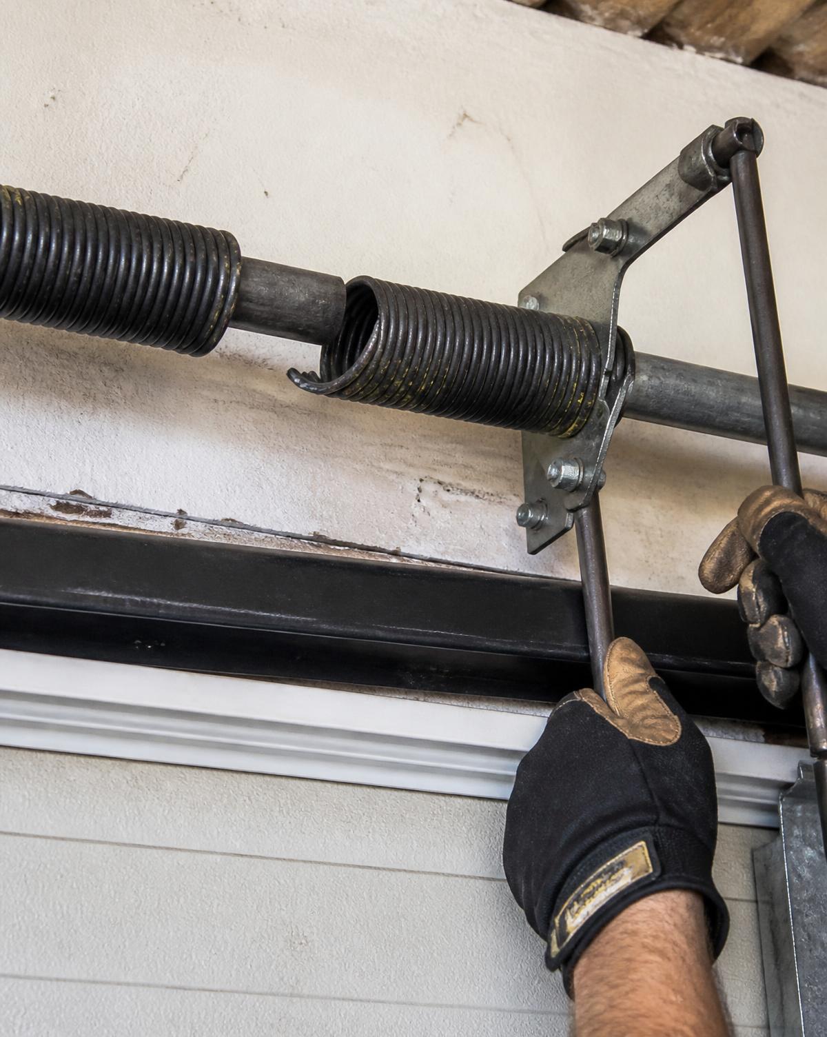 Technician replacing a broken garage door torsion spring with winding bars