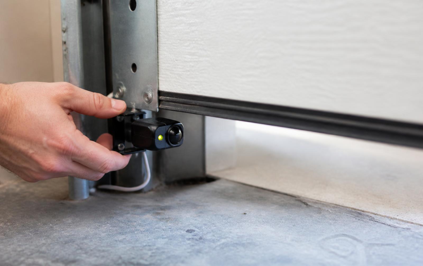 Technician aligning a garage door photo eye safety sensor near the floor